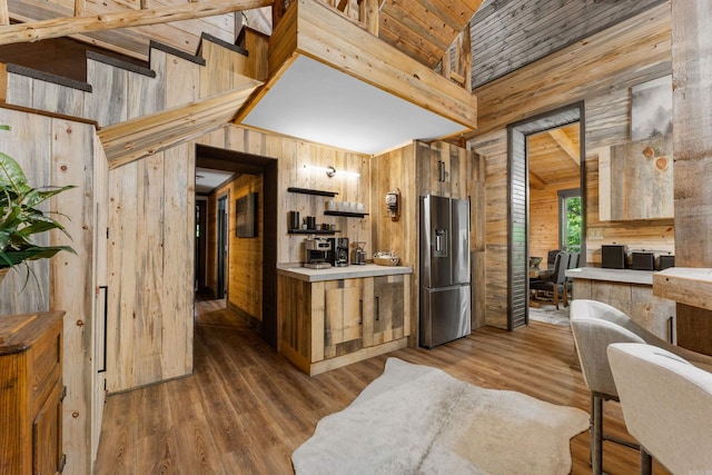 kitchen featuring wooden walls, stainless steel fridge, light countertops, high vaulted ceiling, and wood finished floors
