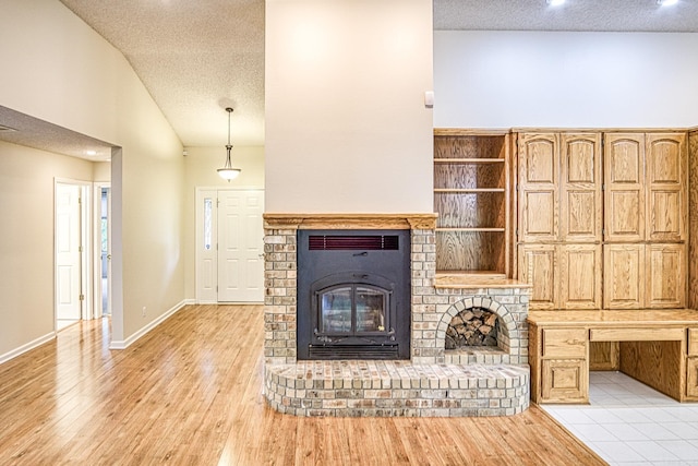 unfurnished living room featuring light wood-type flooring, a textured ceiling, a brick fireplace, and baseboards