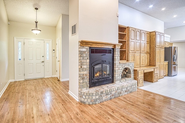 unfurnished living room featuring baseboards, a fireplace, light wood-type flooring, and a textured ceiling