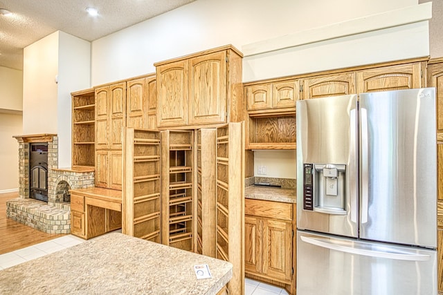 kitchen featuring a textured ceiling, open shelves, light countertops, stainless steel fridge, and light tile patterned flooring