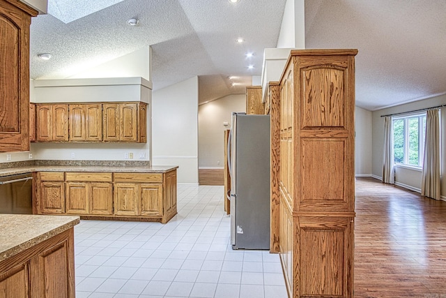 kitchen featuring appliances with stainless steel finishes, brown cabinets, lofted ceiling with skylight, and a textured ceiling