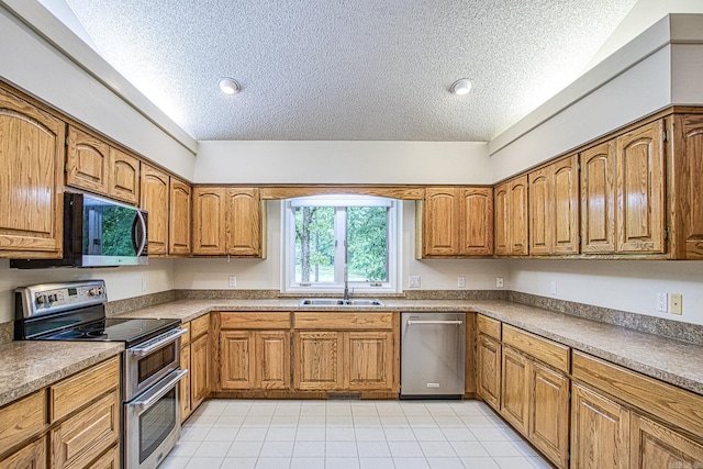 kitchen with a sink, appliances with stainless steel finishes, brown cabinetry, and a textured ceiling