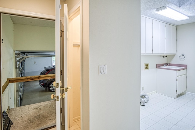 washroom featuring light tile patterned flooring, baseboards, a sink, cabinet space, and washer hookup