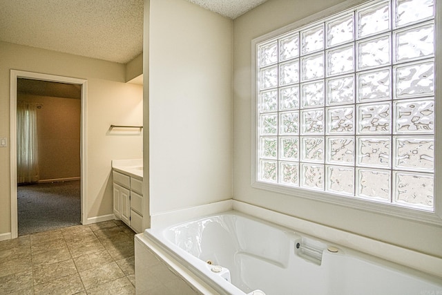 full bath featuring a jetted tub, a textured ceiling, tile patterned flooring, and vanity