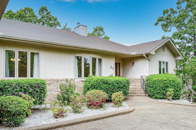ranch-style house featuring roof with shingles, a chimney, and brick siding