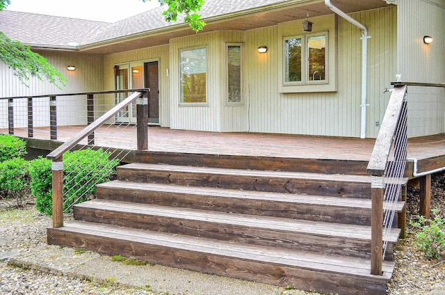 entrance to property with a shingled roof and a deck