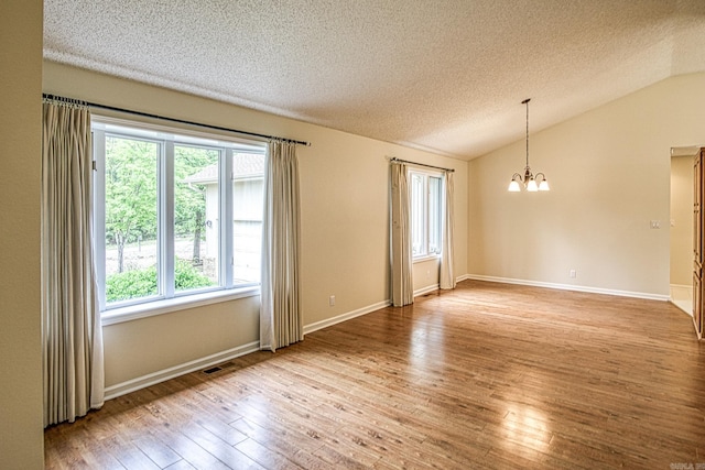 spare room featuring a textured ceiling, a chandelier, vaulted ceiling, light wood-type flooring, and visible vents