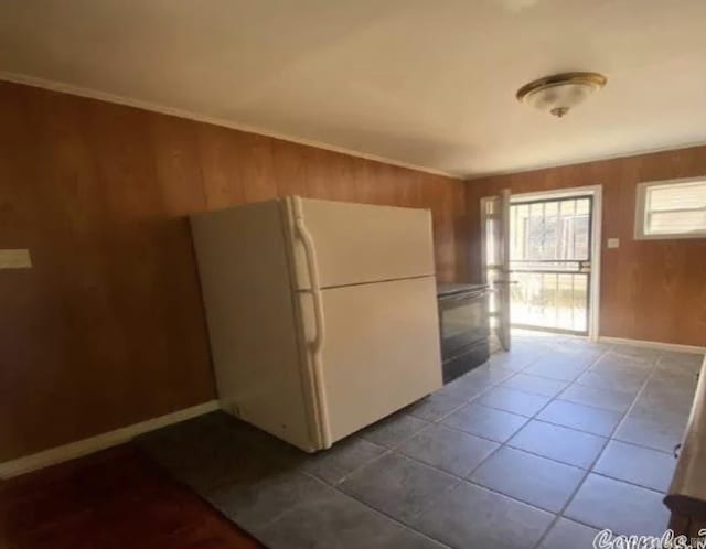 kitchen featuring baseboards, freestanding refrigerator, tile patterned floors, and wood walls
