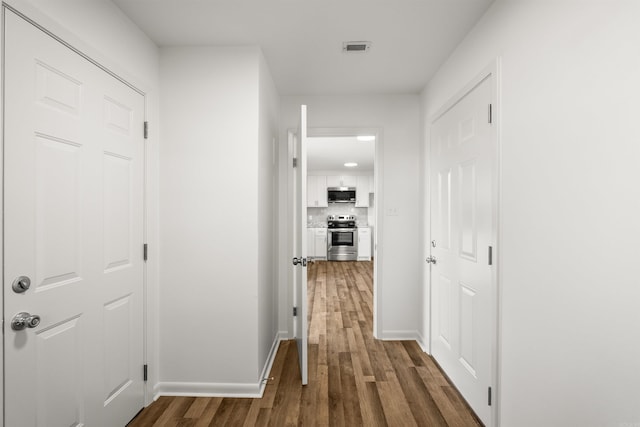 hall with dark wood-style flooring, baseboards, and visible vents