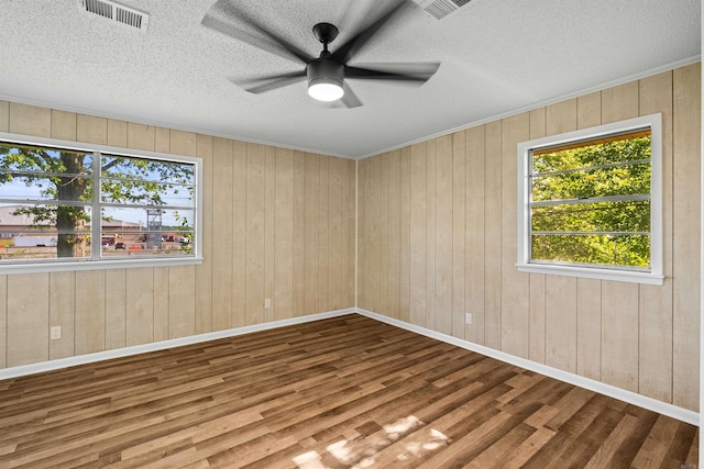 empty room with a ceiling fan, visible vents, a healthy amount of sunlight, and wood finished floors