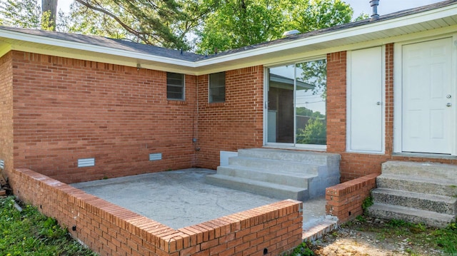view of exterior entry with brick siding and a patio area