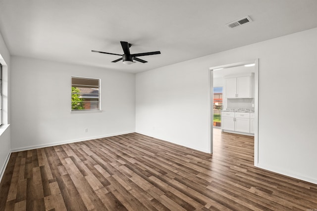 spare room with dark wood-style flooring, a ceiling fan, visible vents, and baseboards