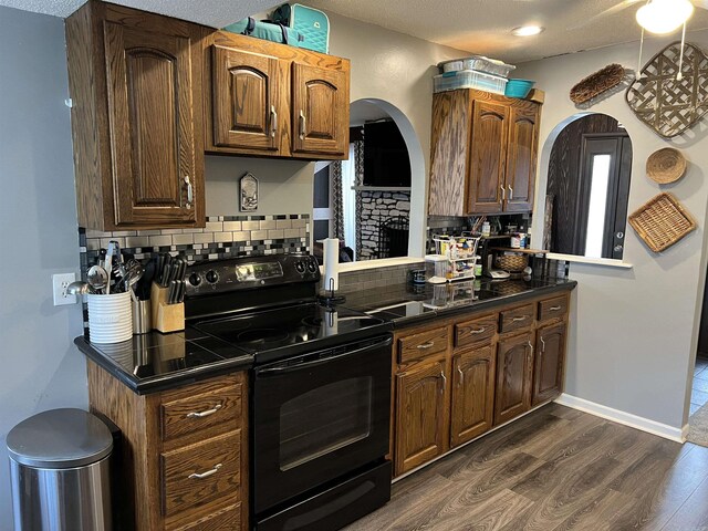 kitchen with black electric range oven, dark wood-style floors, dark countertops, and tasteful backsplash