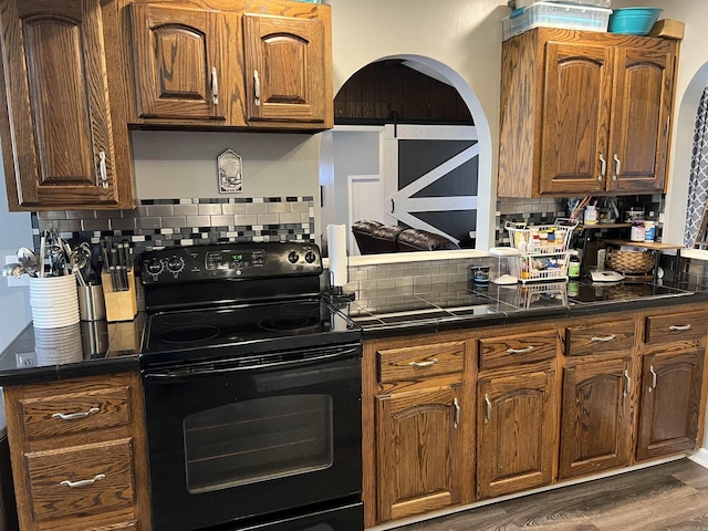 kitchen featuring dark countertops, a barn door, black electric range oven, tasteful backsplash, and dark wood-style floors