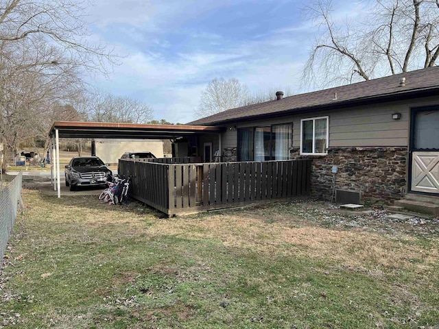 rear view of house featuring a yard, fence, stone siding, and a carport