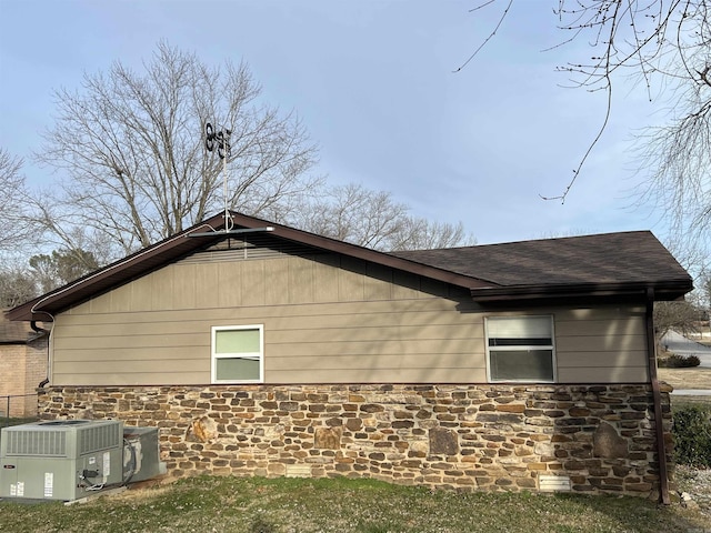 view of property exterior featuring roof with shingles, central AC unit, and stone siding