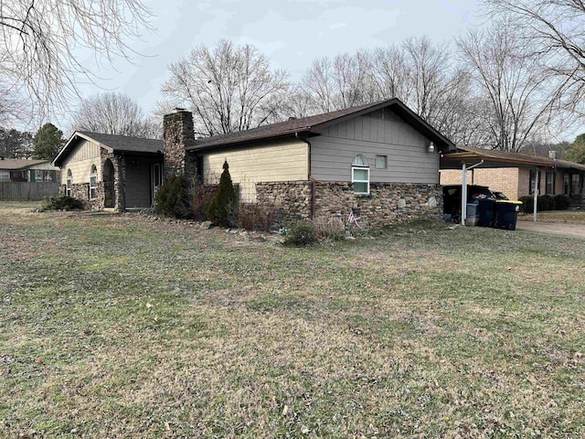 view of side of property with a lawn, a chimney, stone siding, and a carport