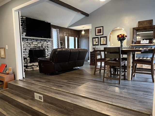 living room featuring visible vents, arched walkways, a fireplace, wood finished floors, and vaulted ceiling with beams