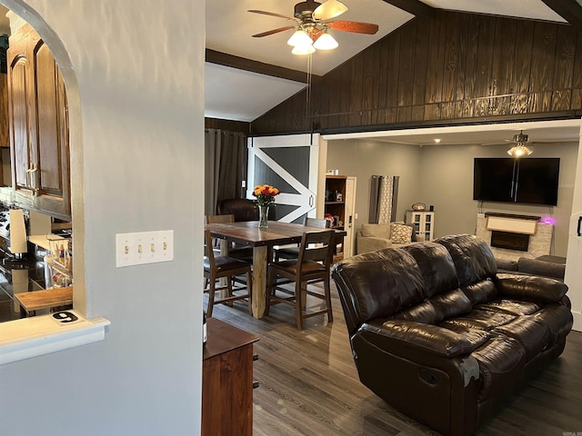 living room with a ceiling fan, dark wood-style flooring, arched walkways, a barn door, and wooden walls