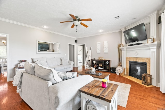 living room with crown molding, light wood-style floors, ceiling fan, recessed lighting, and a tiled fireplace