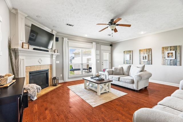 living area with ceiling fan, a textured ceiling, a tile fireplace, visible vents, and dark wood-type flooring
