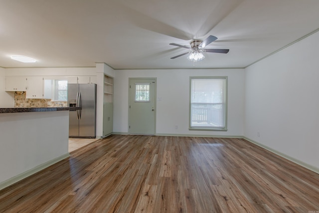 unfurnished living room with a ceiling fan, baseboards, and light wood-style floors
