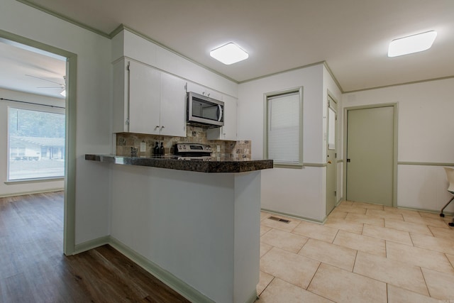 kitchen with decorative backsplash, visible vents, dark countertops, appliances with stainless steel finishes, and a peninsula