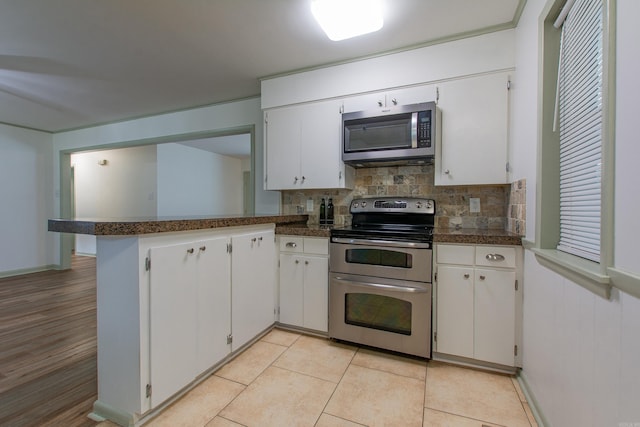 kitchen featuring a peninsula, backsplash, white cabinets, and stainless steel appliances