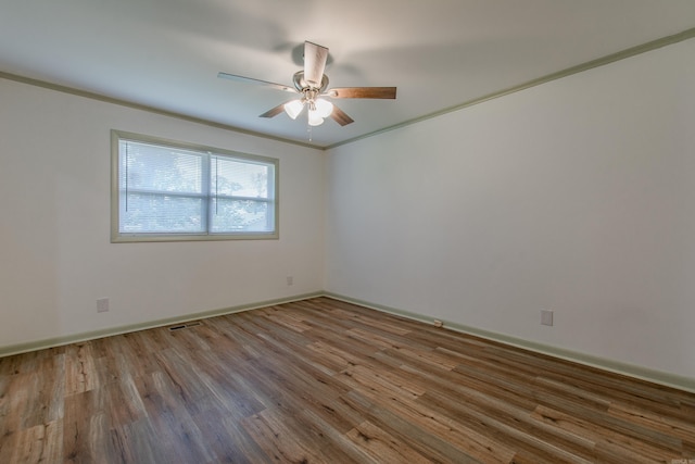 empty room featuring a ceiling fan, visible vents, ornamental molding, and wood finished floors