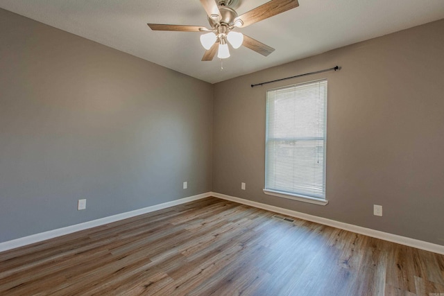 empty room with baseboards, ceiling fan, wood finished floors, and visible vents