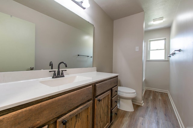 bathroom featuring vanity, wood finished floors, toilet, baseboards, and a bath