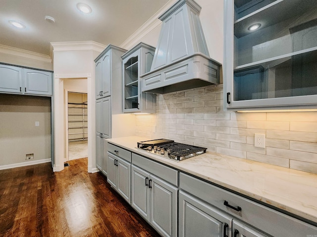 kitchen featuring crown molding, stainless steel gas stovetop, custom range hood, gray cabinetry, and glass insert cabinets
