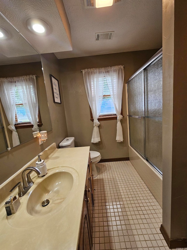 bathroom with visible vents, vanity, toilet, bath / shower combo with glass door, and a textured ceiling