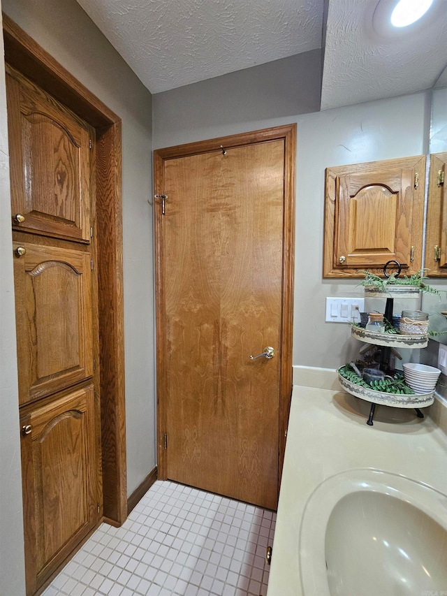 full bathroom with a textured ceiling, tile patterned floors, and a sink