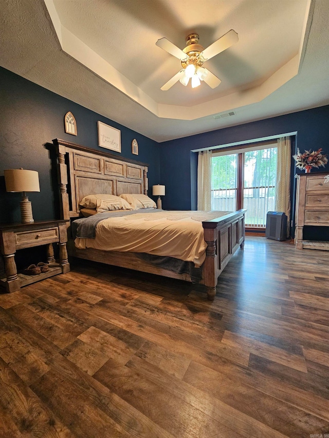 bedroom with a raised ceiling, access to exterior, a ceiling fan, wood finished floors, and visible vents