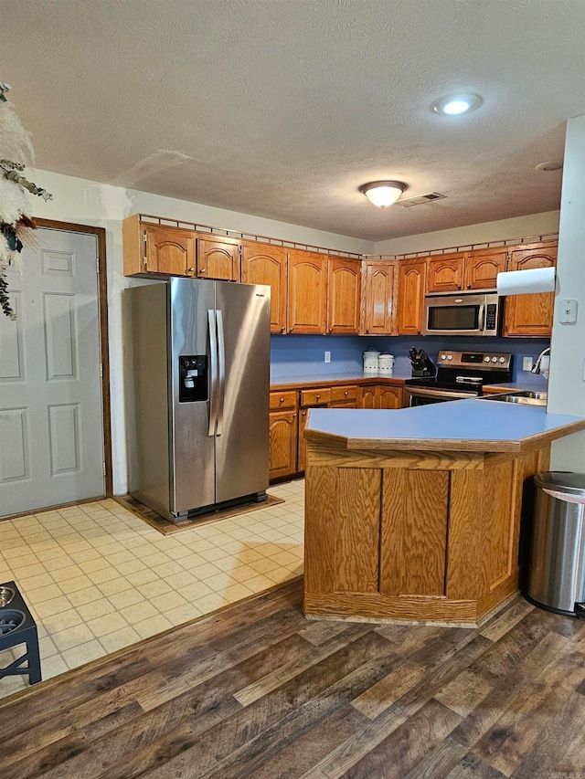 kitchen with brown cabinetry, a peninsula, a textured ceiling, a sink, and stainless steel appliances