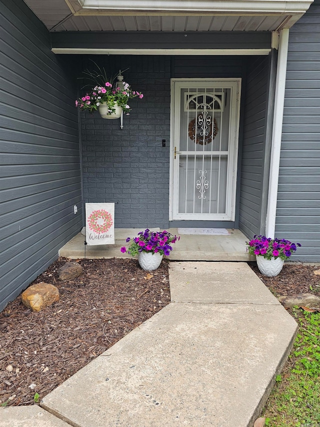 doorway to property featuring a porch and brick siding