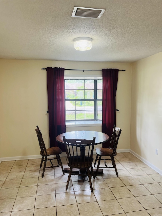 dining space featuring light tile patterned floors, baseboards, a textured ceiling, and visible vents