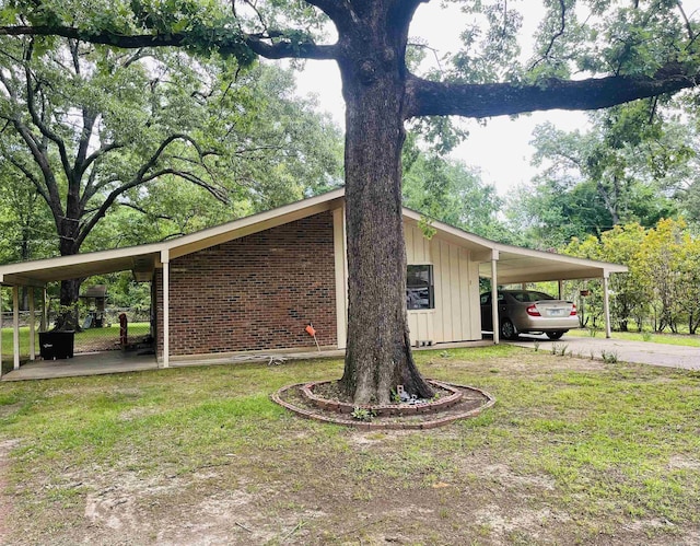 view of home's exterior featuring brick siding, board and batten siding, a lawn, a carport, and driveway