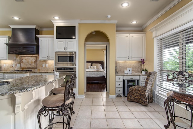 9241 Johnson Dr, Sherwood, AR 72120 - kitchen with light stone countertops, beverage cooler, a breakfast bar area, premium range hood, and appliances with stainless steel finishes