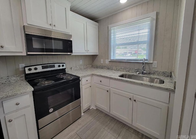 kitchen featuring white cabinets, light stone countertops, a sink, wood walls, and stainless steel appliances