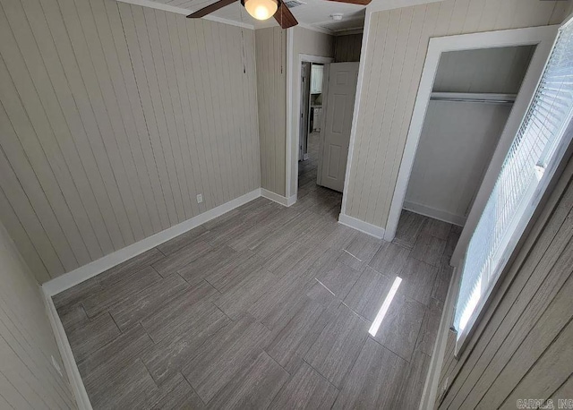 unfurnished bedroom featuring a closet, wood walls, crown molding, baseboards, and a ceiling fan