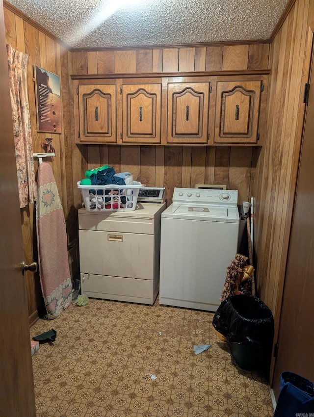 washroom featuring washer and clothes dryer, cabinet space, a textured ceiling, and wooden walls