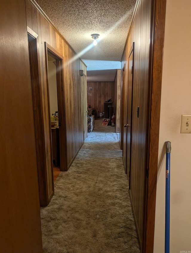 corridor with wood walls, dark carpet, and a textured ceiling