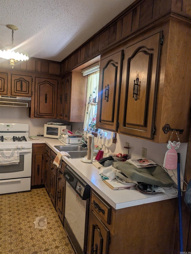 kitchen featuring a textured ceiling, light countertops, a sink, under cabinet range hood, and white appliances
