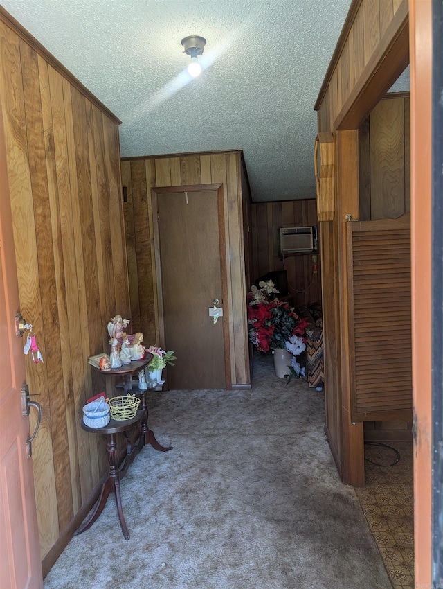 hallway with an AC wall unit, a textured ceiling, wood walls, and carpet