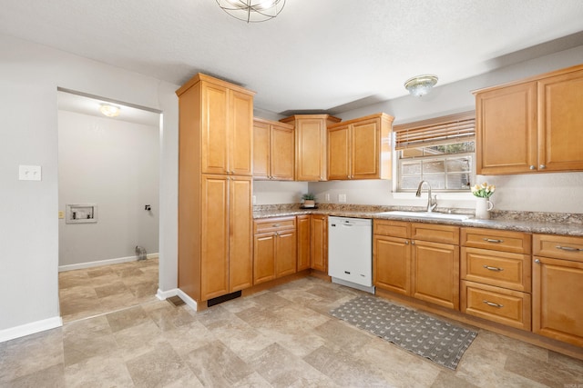 kitchen featuring white dishwasher, baseboards, stone finish flooring, and a sink
