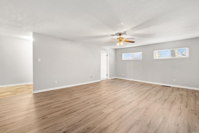 empty room with ceiling fan, a textured ceiling, visible vents, wood finished floors, and baseboards