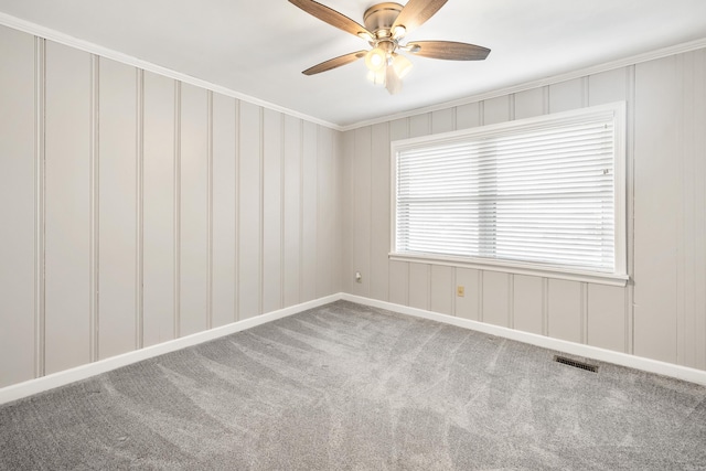 carpeted empty room with baseboards, ornamental molding, a ceiling fan, and visible vents