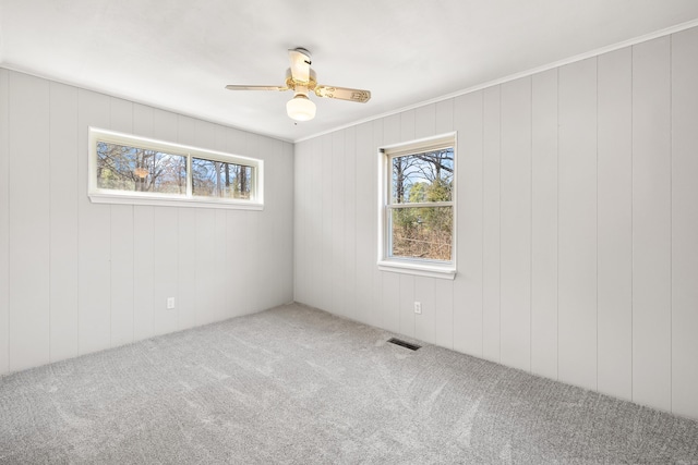 empty room with carpet floors, a ceiling fan, crown molding, and visible vents